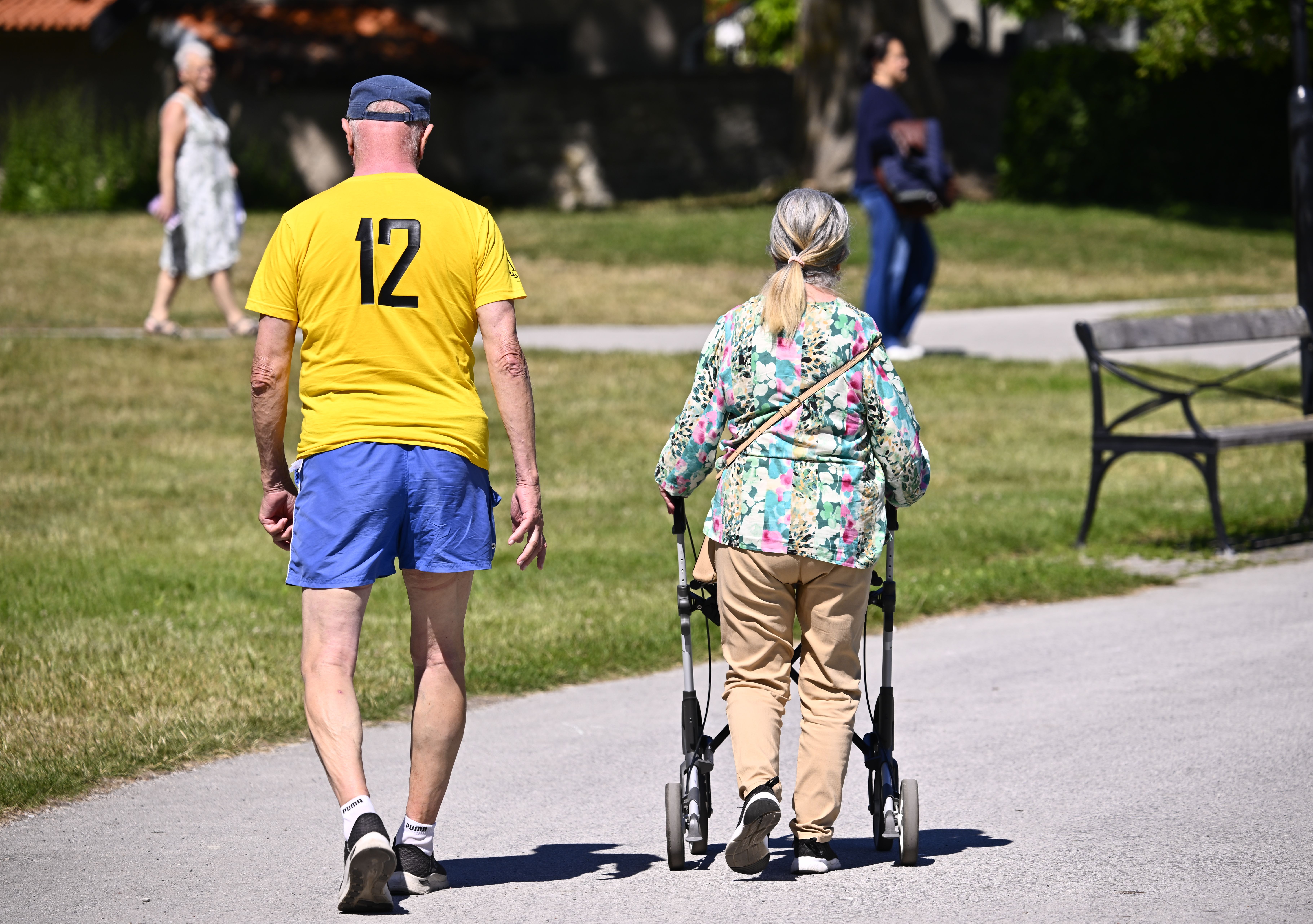 Två pensionärer som går på en asfalterad gata i sommaren.